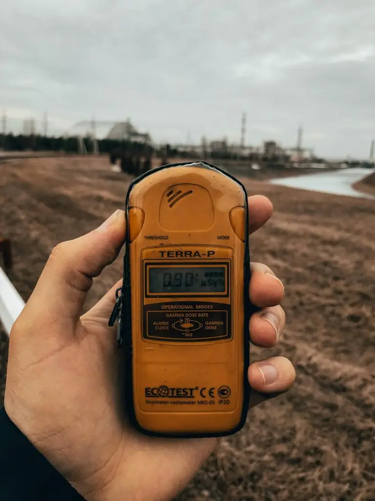 Hand holding a Terra-P dosimeter in an outdoor setting measuring radiation levels.